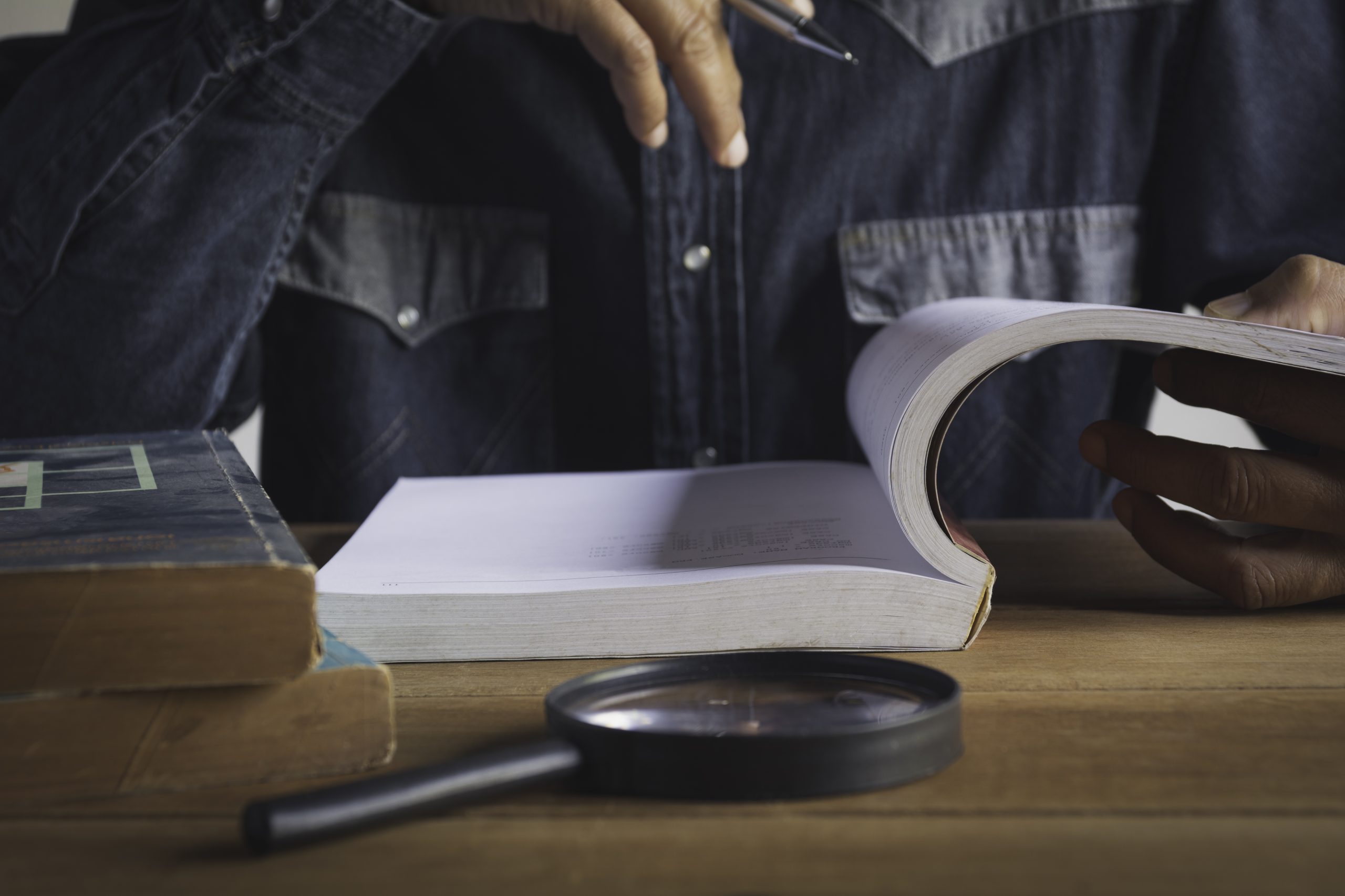 homem lendo um livro sobre uma mesa com uma lupa em frente ao livro