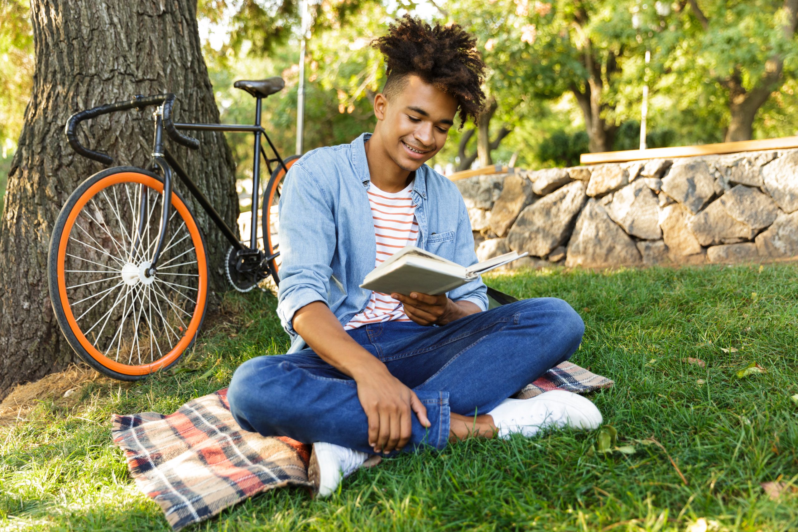 jovem adulto sentado em um parque arborizado lendo um livro