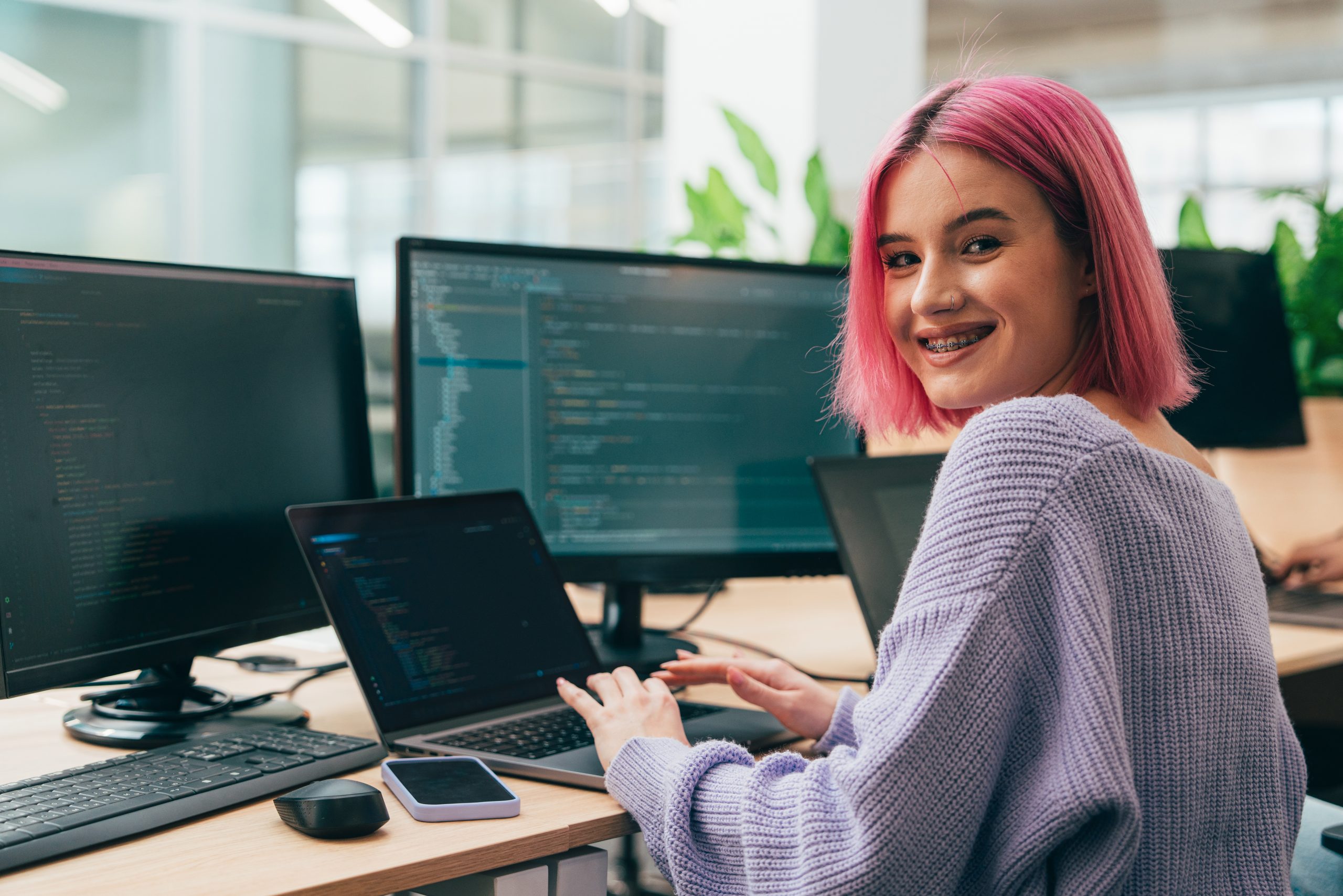 jovem adulta sentada em frente a três computadores programando