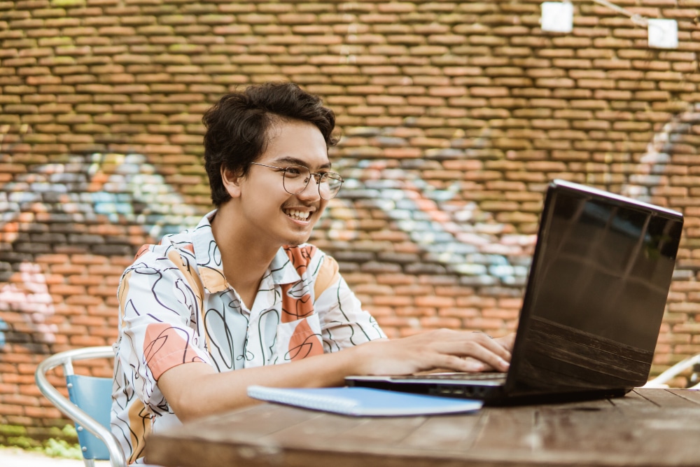 jovem adulto sentado em ambiente externo usando notebook