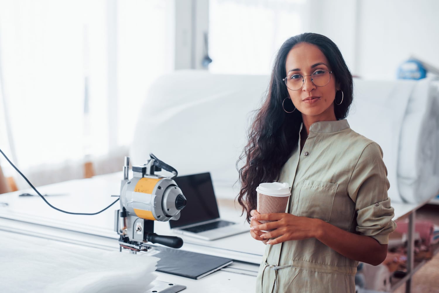 Mulher empreendedora, com um copo na mão, em frente a uma máquina.