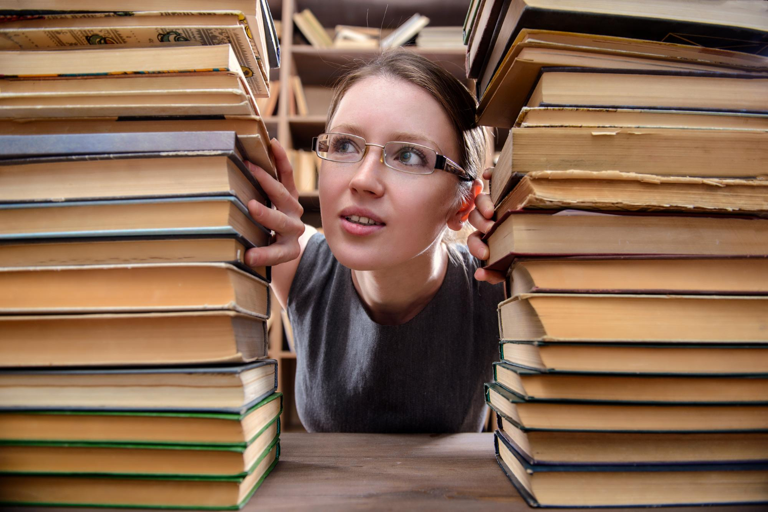 Mulher usando óculos e ao seu redor há muitos livros empilhados sobre PNL