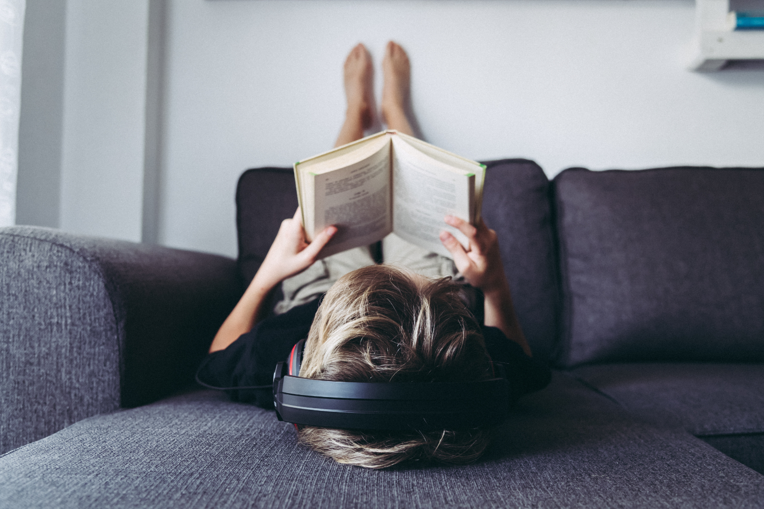 Mulher deitada no sofá, lendo livro.