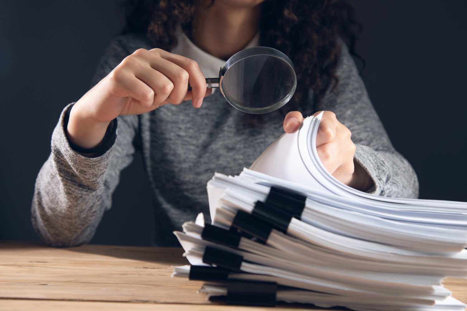 Mulher com uma lupa, analisando documentos.