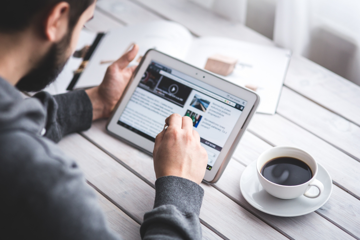 homem sentado com um tablet em mãos se atualizando de notícias. ao seu lado uma xícara de café