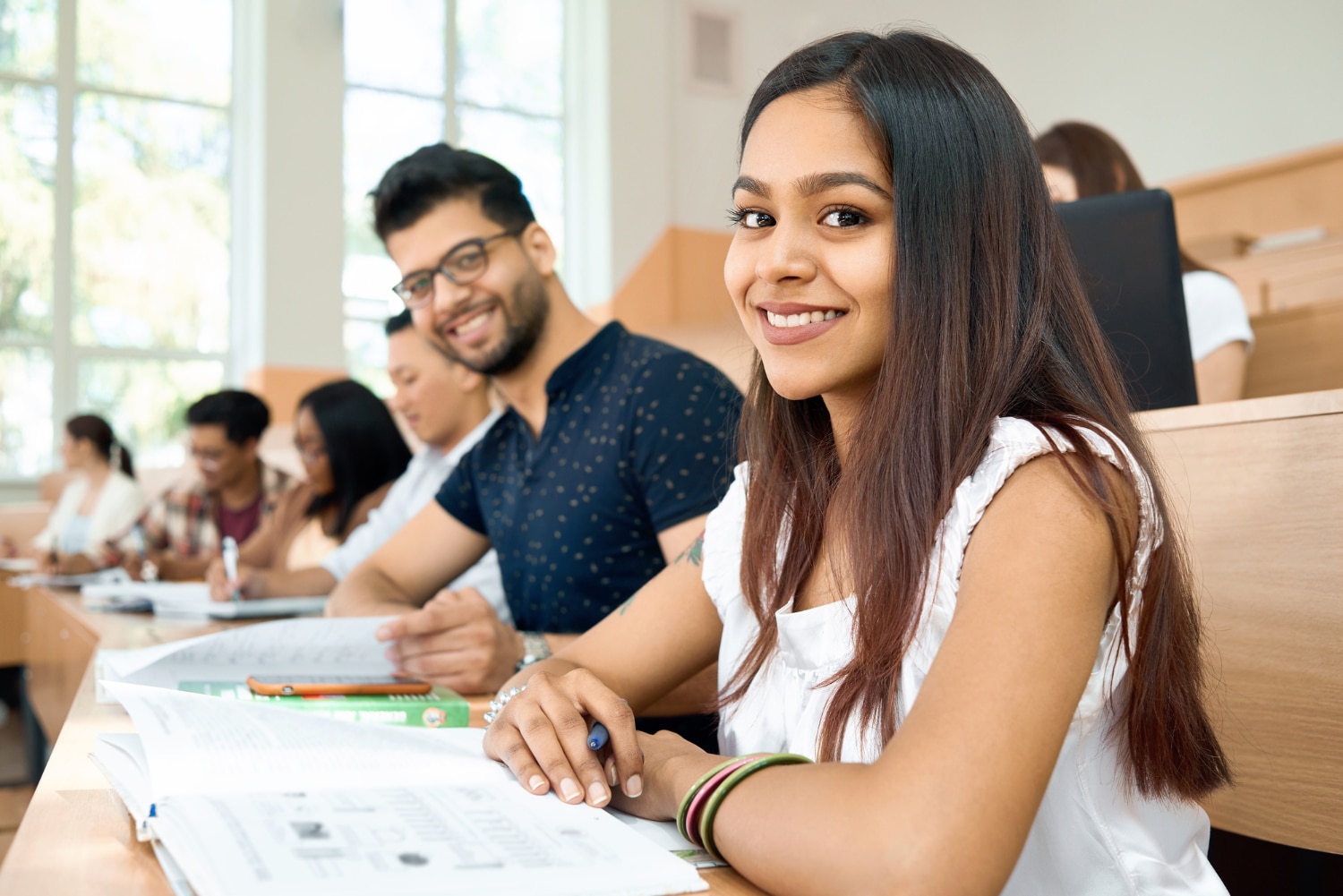 alunos em sala de aula sorrindo para a câmera, com cadernos abertos sobre a mesa