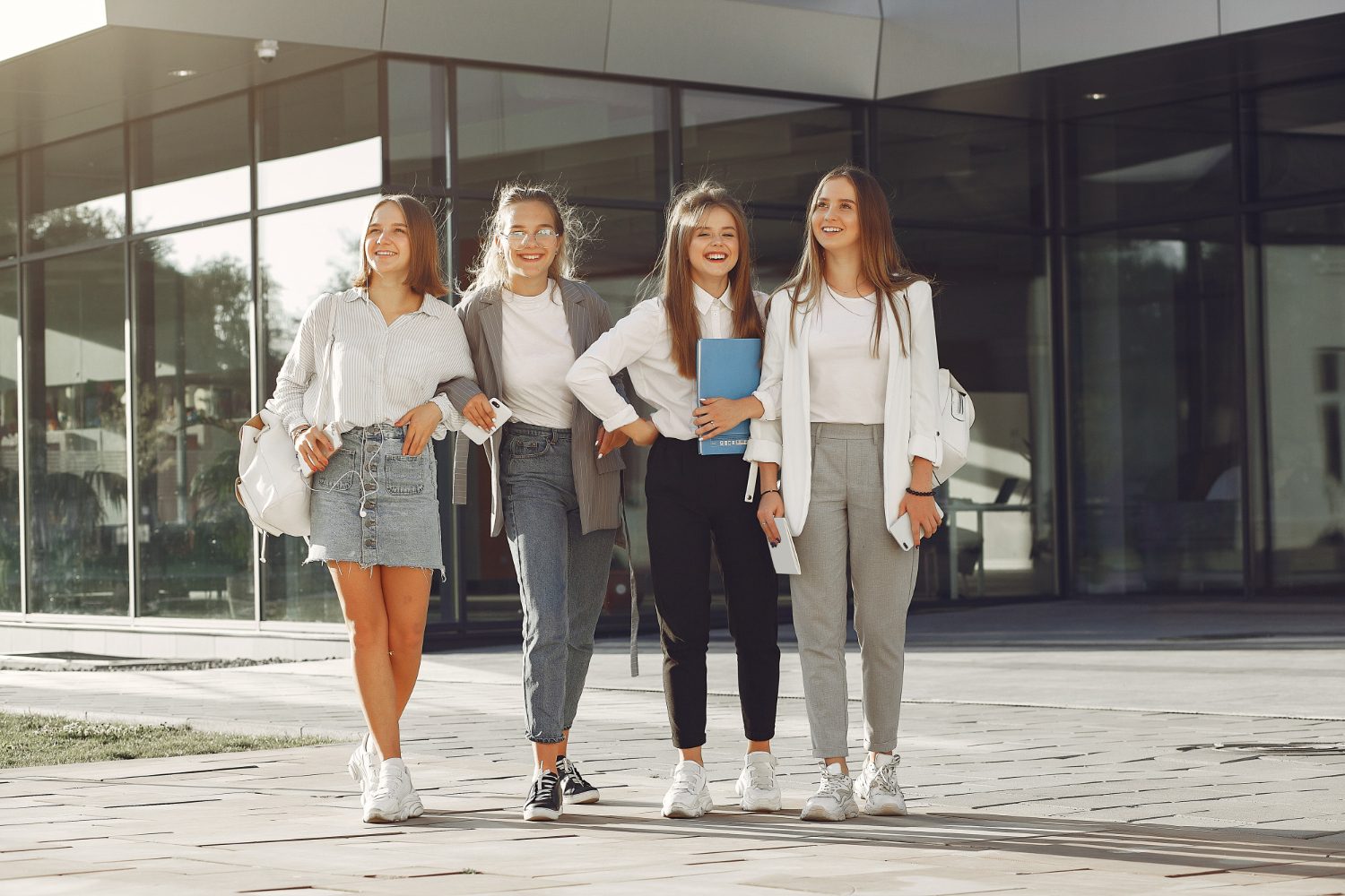 grupo de jovens adultas em pé diante de um prédio que remete a faculdade. Todas estão sorrindo lado a lado