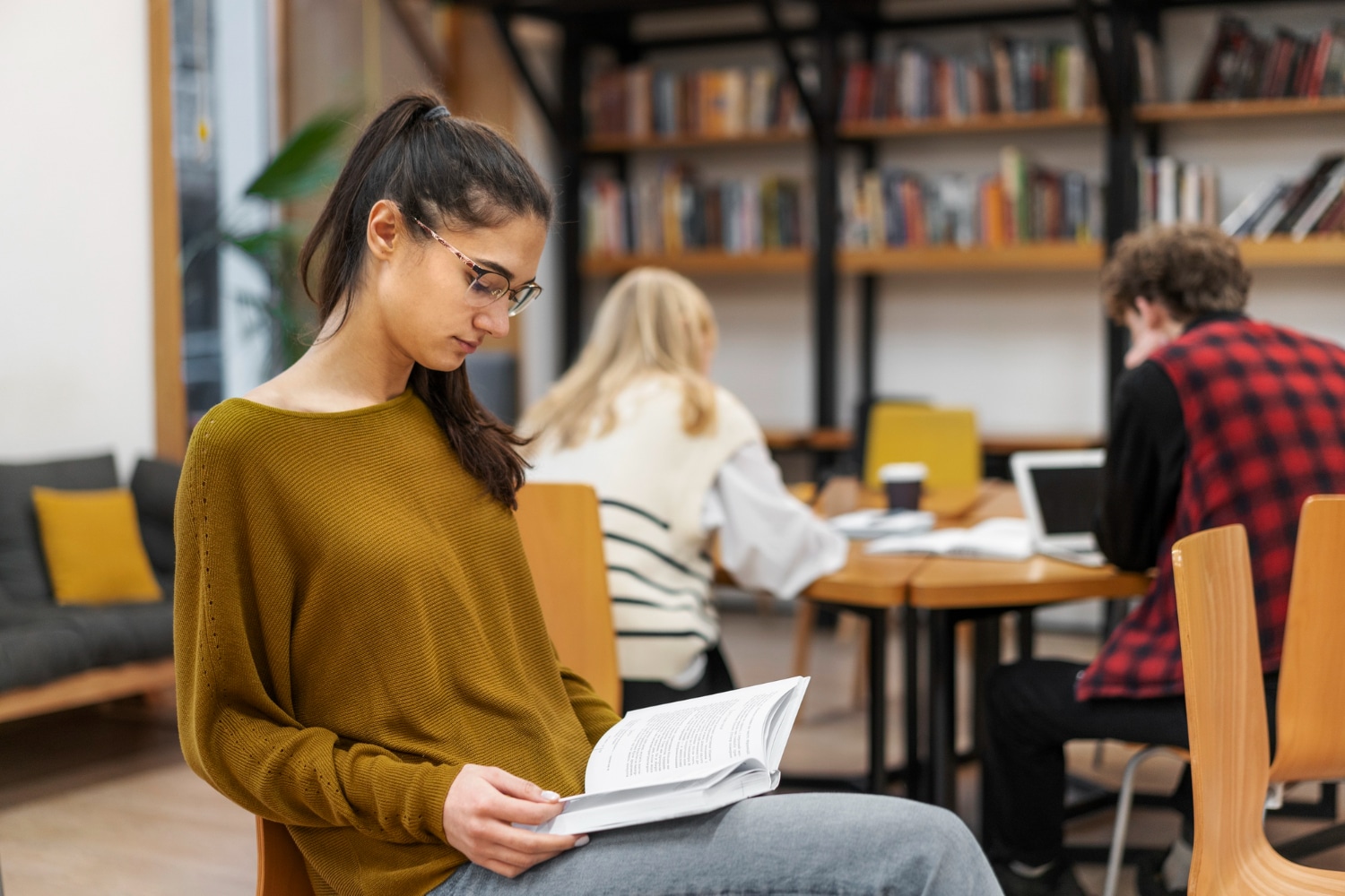 jovem adulta sentada lendo um livro na biblioteca