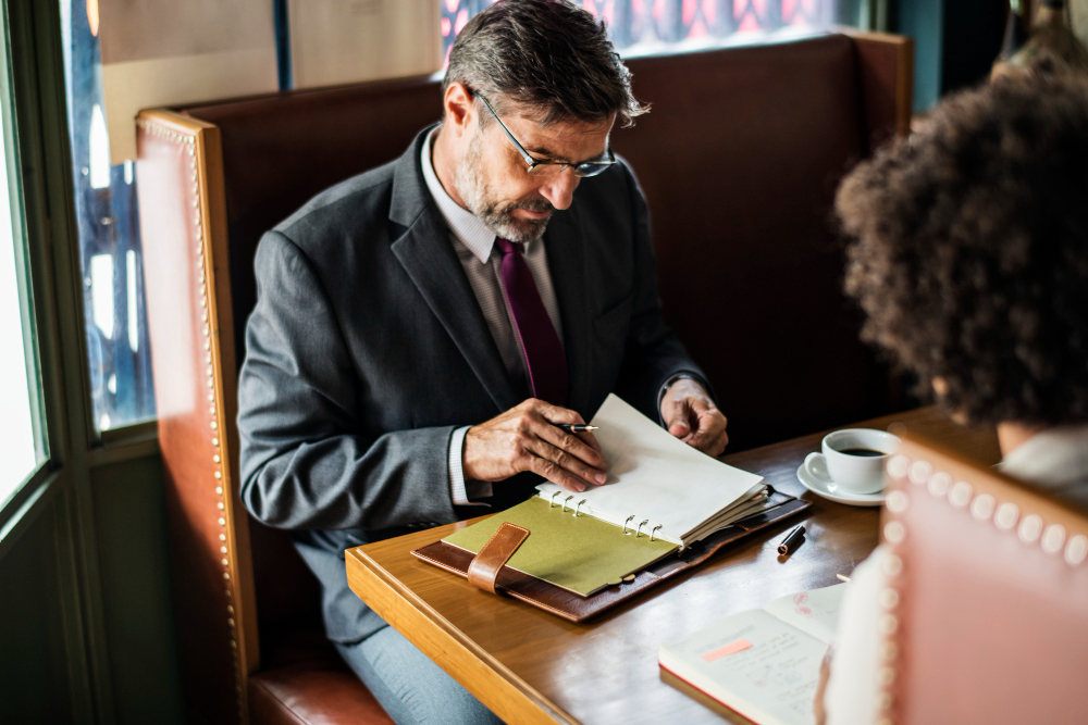 Homem em frente a uma mesa com uma agenda, atendendo um cliente.