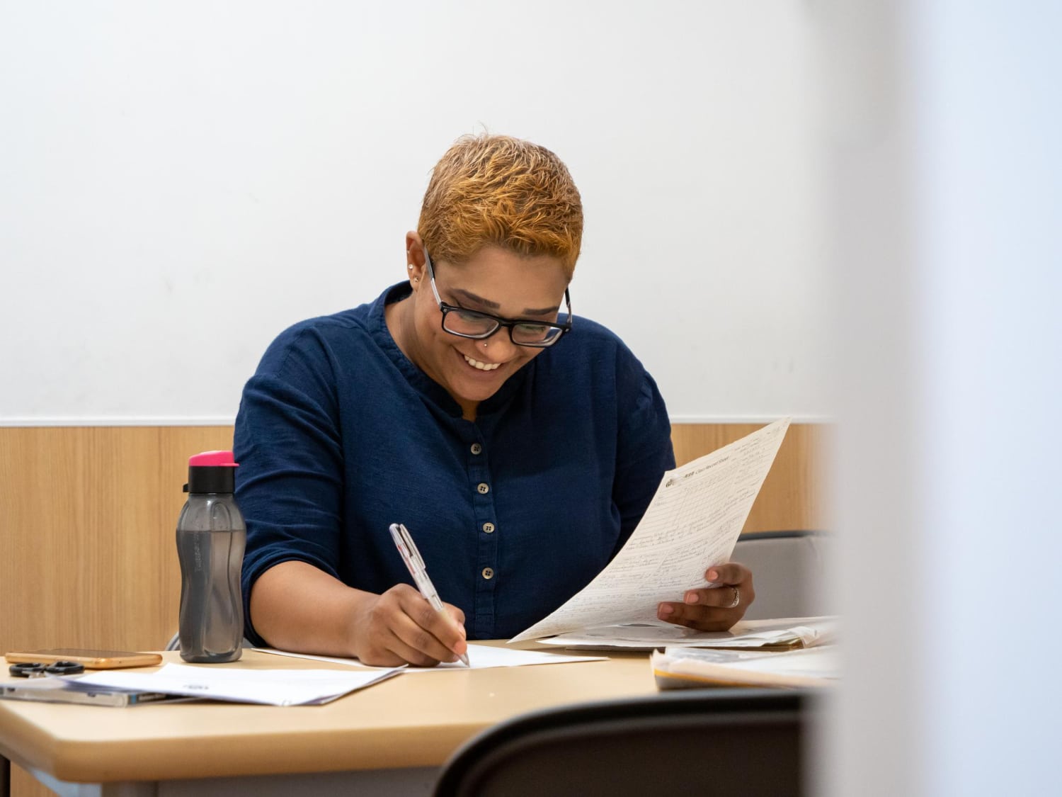 mulher estudando para prova. Com cadernos e anotações sobre a mesa. Ao lado, uma garrafinha de água