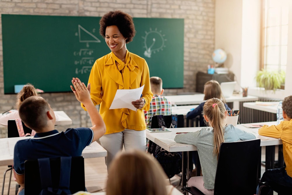 Professora em frente a lousa, dando aula, com vários alunos.