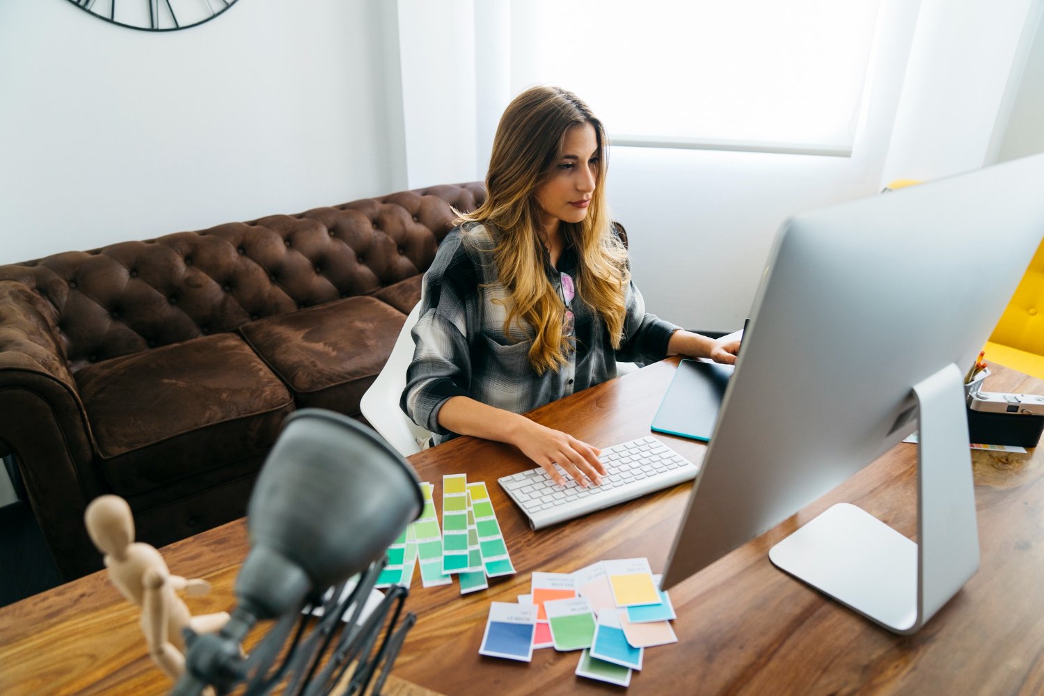 Designer feminina trabalhando em um computador no escritório, sobre a mesa ao seu lado varios cards com paleta de cores